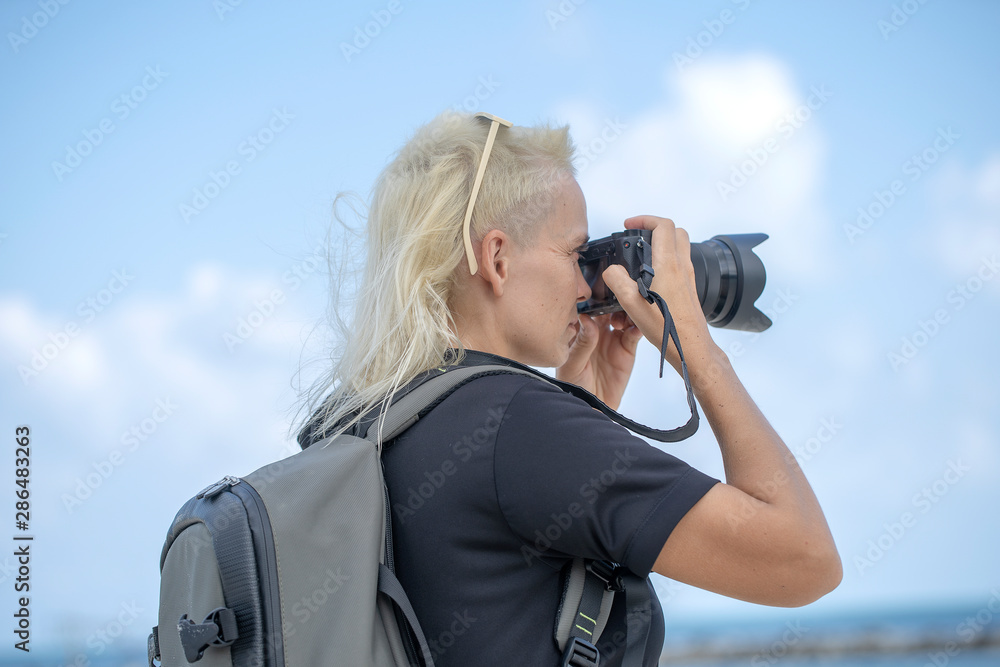 Tourist traveler photographer taking pictures of landscape on photo camera , hipster girl with backpack enjoying beautiful sea landscape. Close up portrait young tourist of a blonde girl