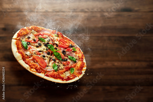 Pizza on a wooden background with ham, olives, tomatoes and green basil. Itolyan cuisine, copy space.