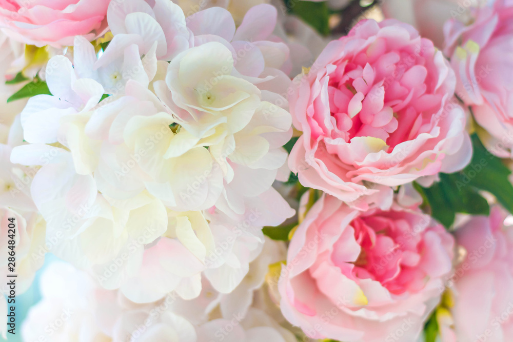 Artificial pink peonies and lilacs lit by the sun on a blue background.