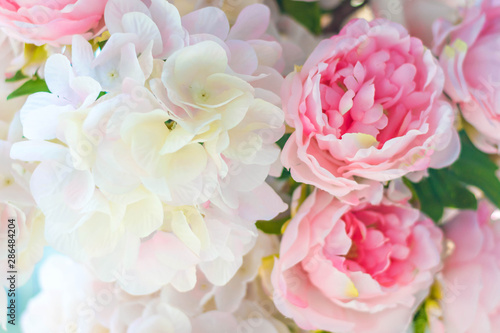 Artificial pink peonies and lilacs lit by the sun on a blue background.