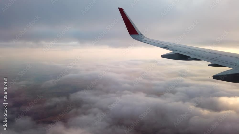 View from the porthole of an airplane. Flying at high altitude over an even layer of clouds. Early morning.