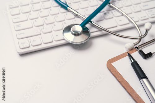 Doctor diagnoses concept - stethoscope on computer keyboard with medical record case and pen on white working table. Top view, flat lay, copy space