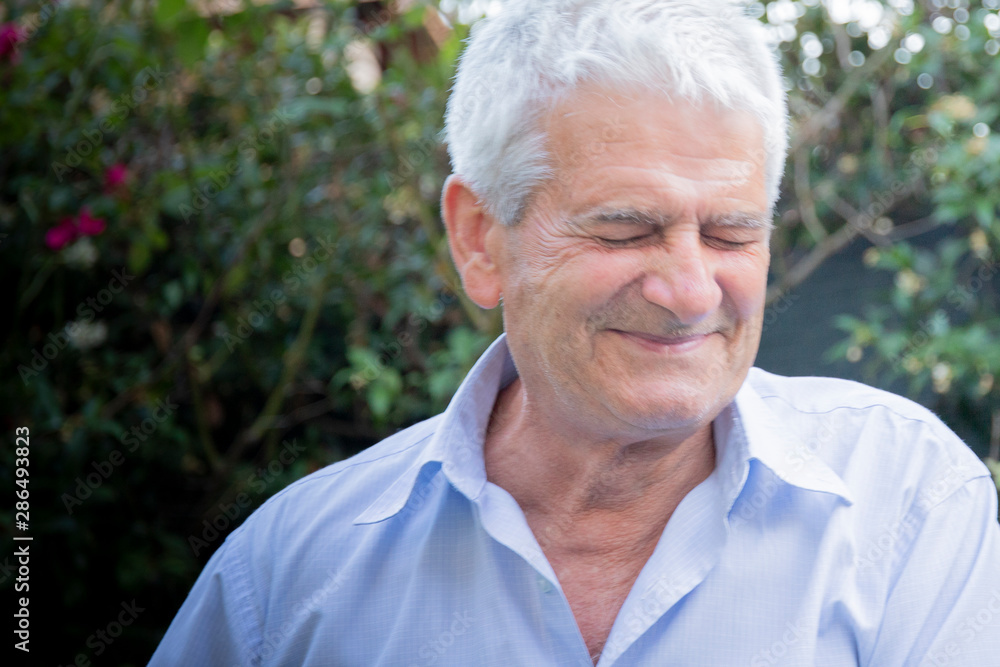 Older white man with grey hair, wearing a shirt, smiling with closed eyes and funny expression in outdoor location with natural light. Copy space on the left. Older white man with grey hair, wearing a shirt, smiling with closed eyes and funny expression in outdoor location with natural light. Copy space on the left.