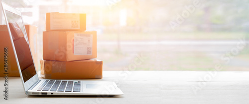 Laptop computer at workplace of start up, small business owner. cardboard parcel box of product for deliver to customer. Online selling, e-commerce, packing concept, Morning light,blurred image photo