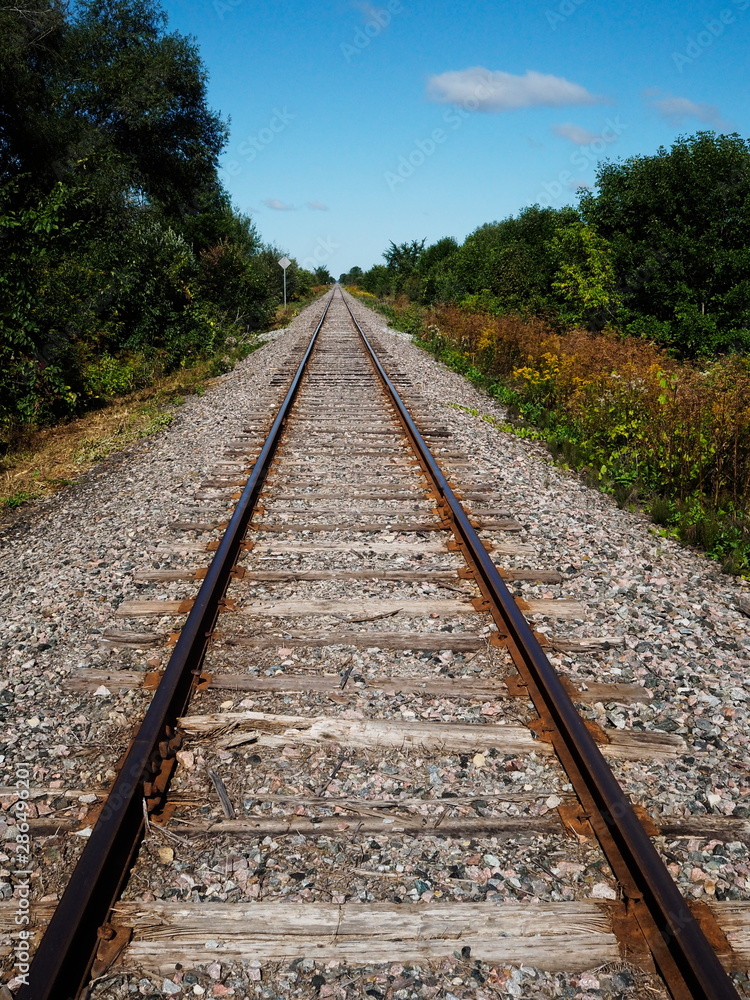Railway tracks in a rural scene with a bright blue sky and white clouds. Tracks disappear into the distance. Railway tracks in a rural scene with a bright blue sky and white clouds. Tracks disappear into the distance.