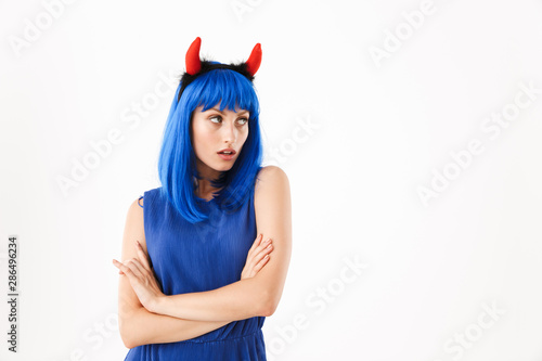 Portrait of cute serious woman wearing blue wig and toy devil horns looking aside at copyspace
