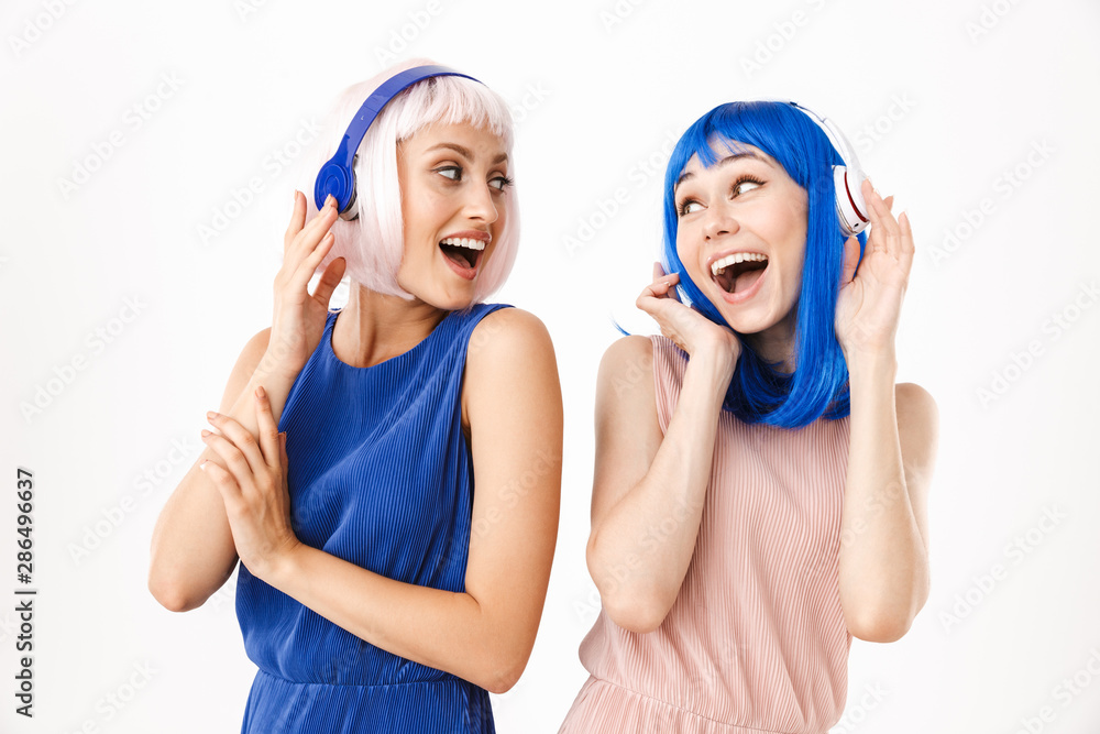 Portrait of two ecstatic women wearing blue and pink wigs listening music with headphones