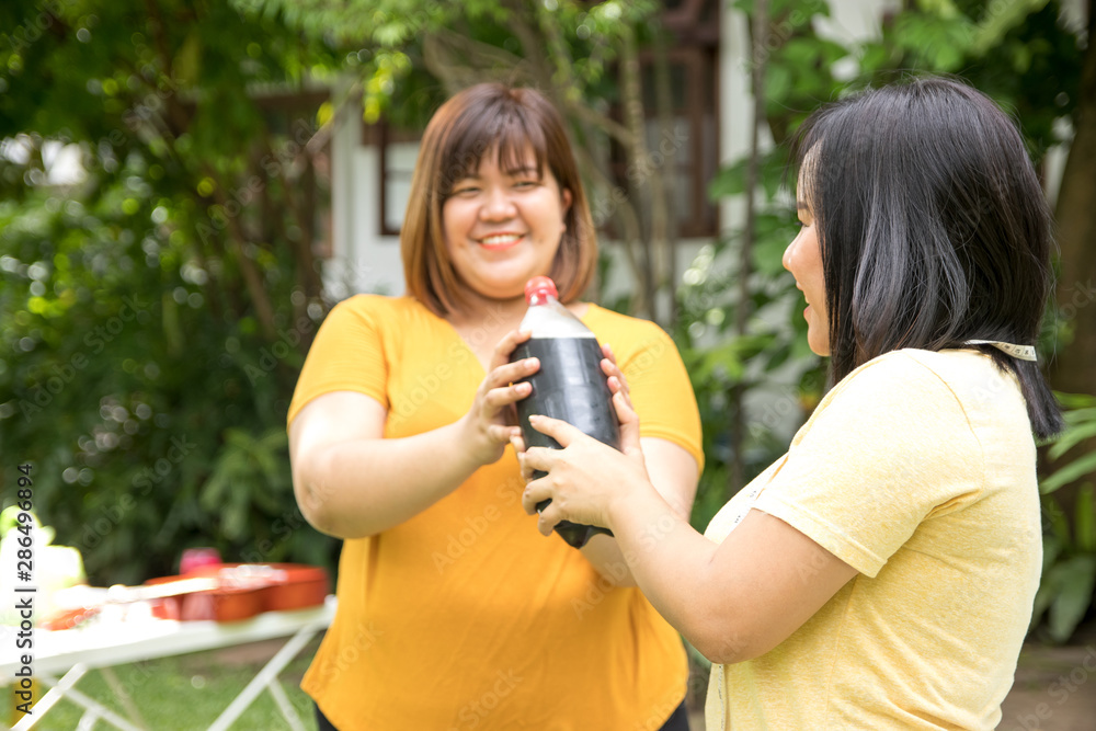 A chubby woman is partying in the front garden with a large bottle of cola drink that she has delivered. They enjoy eating fast food and drinks that are sweet because they feel refreshed.
