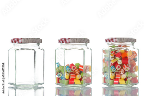 three glass jar, one empty, one half empty and one full of colored candies isolated on white background with clipping path and copy space for your text