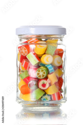 a glass jar half  full of colored candies with copy space isolated on white background with clipping path