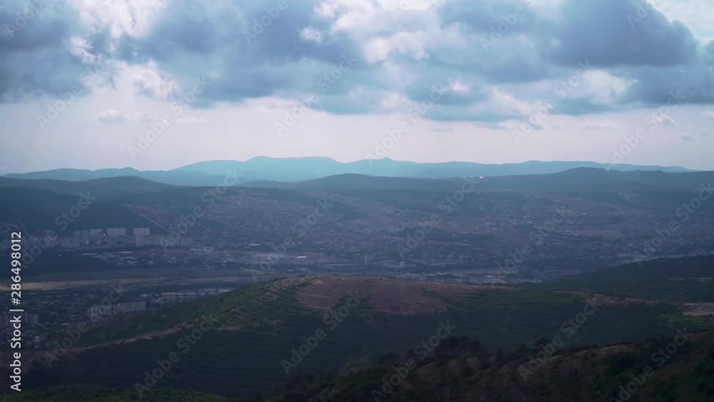 View from the top of the mountains on the green mountains with the city on the horizon on a cloudy day in summer. A bewitching view of the city from above. View from the top of the mountains on the green mountains with the city on the horizon on a cloudy day in summer. A bewitching view of the city from above.