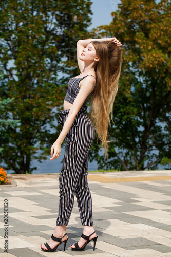 Young beautiful woman in striped trousers walking on the street, summer embankment outdoorst