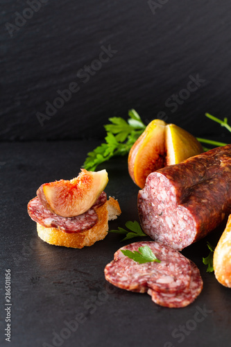 Food concept dried cured sausage on black slate board with copy space