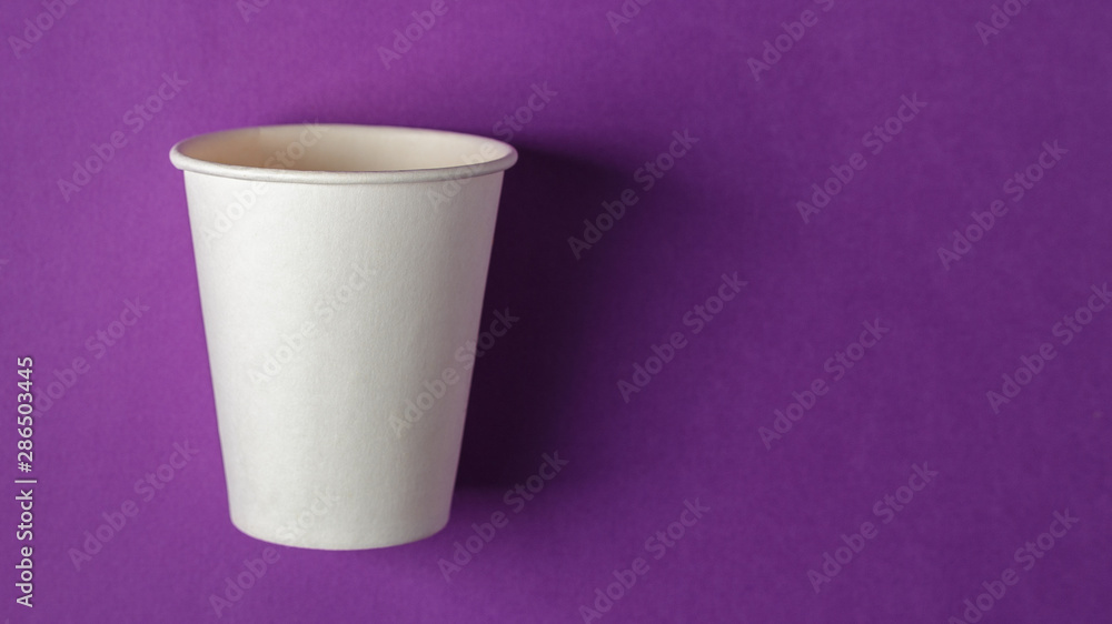 Empty white paper cup on vivid purple background Empty white paper cup on vivid purple background