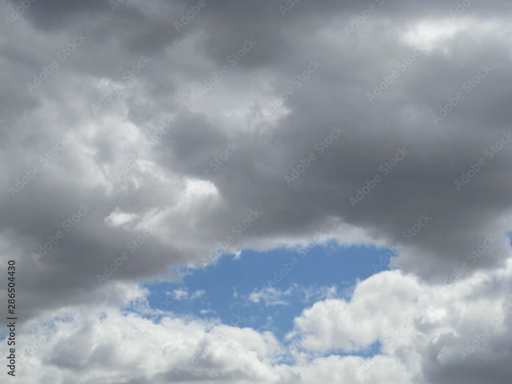 Nubes combinadas: grises arriba más blancas abajo preparando tormenta de primavera con centro de cielo azul aún visible