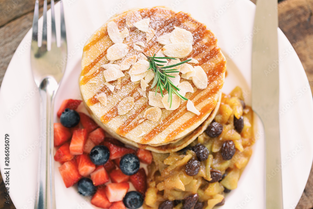 Φωτογραφία Homemade pancake or hot cake stacked on white plate with fresh fruit and apple raisin sauce on wood table