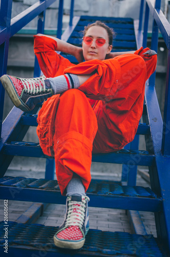 Young woman in red overalls and red sunglasses posing on the blue stairs. Industrial concept