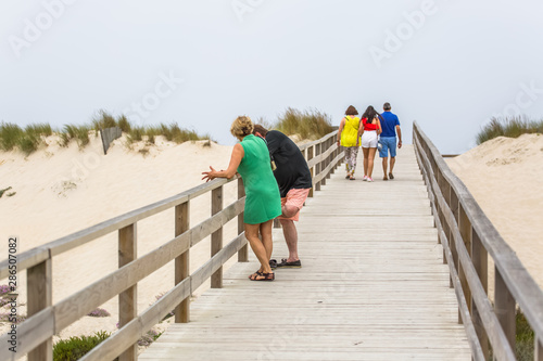 Fototapeta Naklejka Na Ścianę i Meble -  View of pedestrian path on beach, backs of couple with daughter walking on wooden path and other couple talking