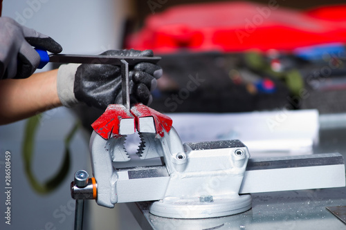 in the photo, a hand in a gray working glove is finalizing a metal workpiece clamped in a vice photo