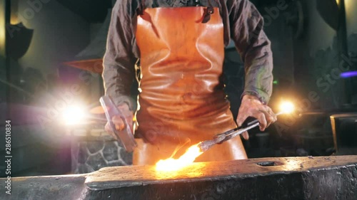 Inflamed metal is getting hammered by the blacksmith. Slow motion.