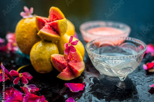 Guava pulp and water well mixed in a glass bowl on the wooden surface along with some raw cut guava, with some rose petals, also completing a face mask used for a natural glow. photo