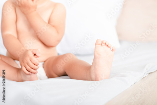 Partial view of little child with tiny toes and fingers sitting on white bed
