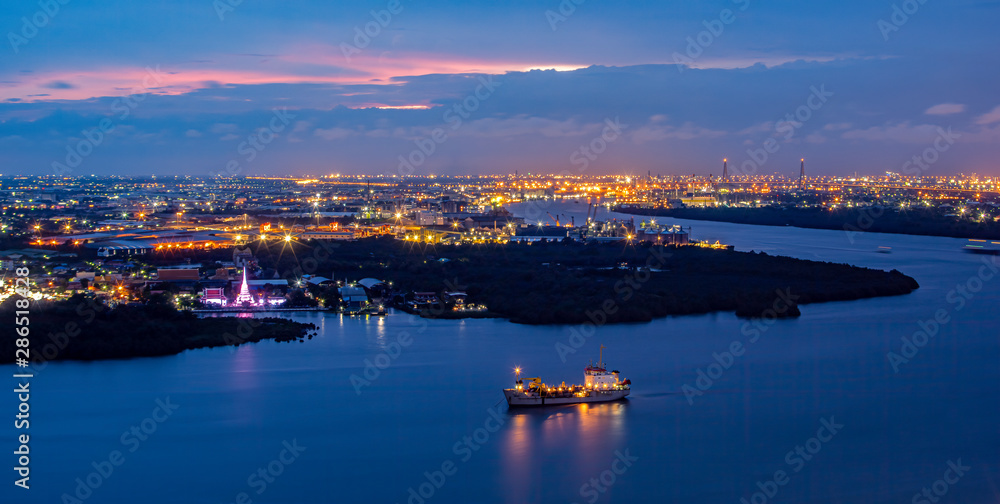 Street lights and street lighting from residential houses in the suburbs during sunset time, boat traffic on the Chao Phraya River, Samut Prakan, Thailand