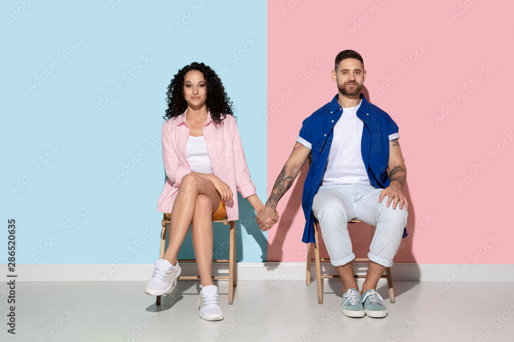 Naklejka premium Young emotional caucasian couple in bright casual clothes posing on pink and blue background. Concept of human emotions, facial expession, relations, ad. Woman and man holding hands, look happy.