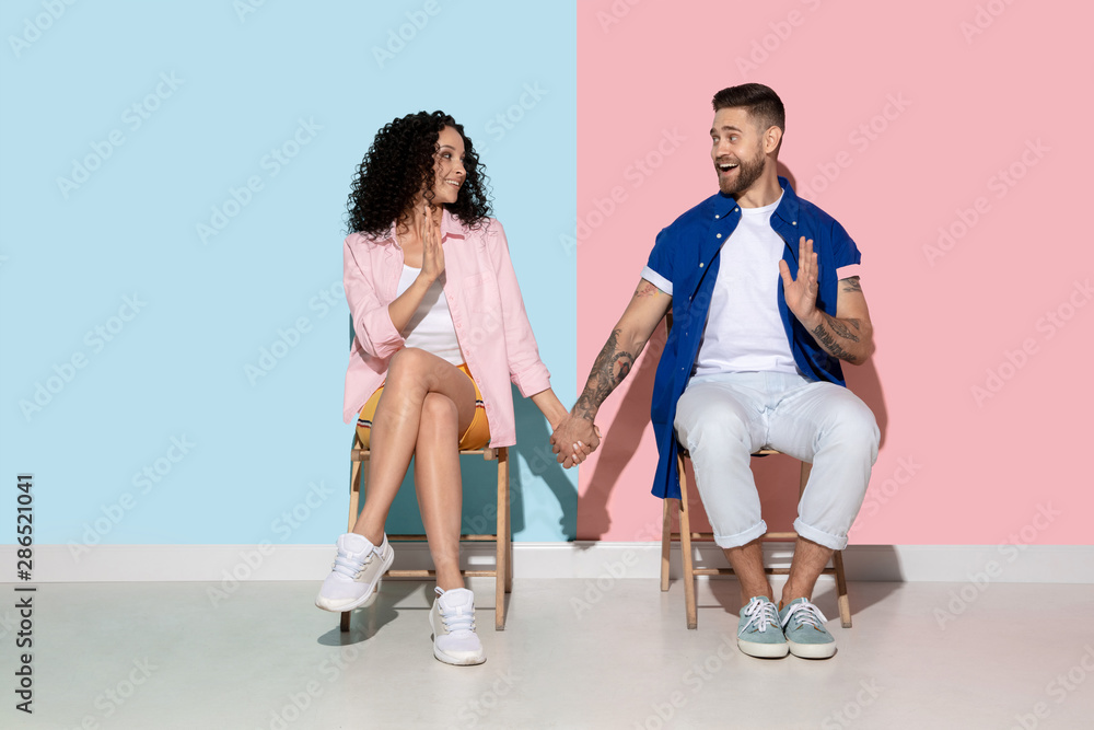 Obraz premium Young emotional caucasian couple in bright casual clothes posing on pink and blue background. Concept of human emotions, facial expession, relations, ad. Woman and man holding hands, look happy.