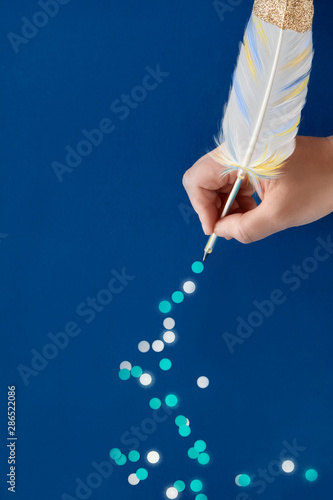 Female hand drawing trail of paper snowflakes from blue feather quill on dark blue paper