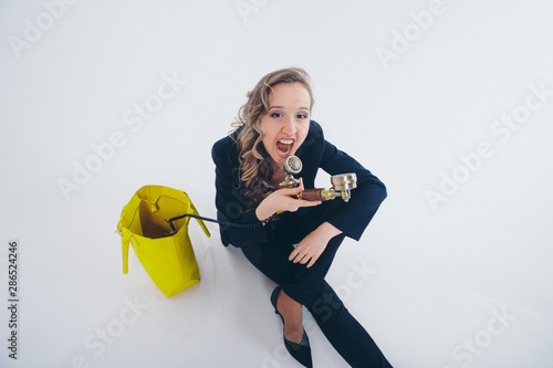 a businesswoman in a black and yellow suit pulls out of a yellow bag phone and yells at him. Beautiful woman sitting on floor on white background. the concept of the work in the office, business plan,