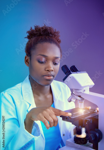 African scientist or graduate student in lab coat works with modern light microscope photo