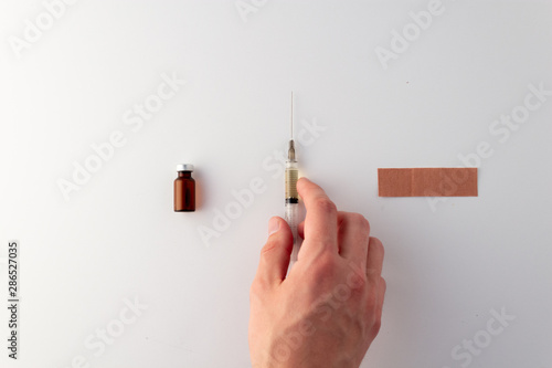 Flat lay of needle, band aid and vial of medicine. Hand reaching for needle. Flu