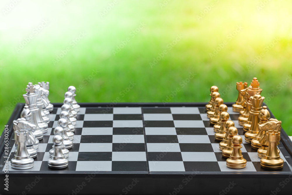 Chess game, set the board waiting to play in both gold and silver pieces on green grass background