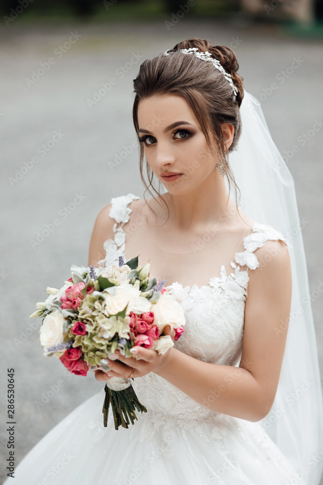 Naklejka premium Beautiful cheerful bride with a bouquet. Beautiful wedding bouquet in hands of the bride. Bride with elegant hairstyle and makeup