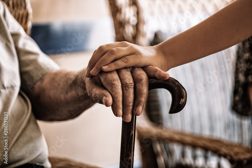 child's hand over old man's hand holding a cane. photo