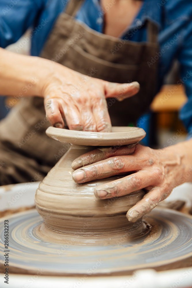 Senior female potter working on pottery wheel while sitting  in her workshop