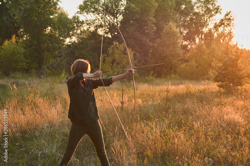 Canvas Print A woman shoots a bow in nature at sunset.