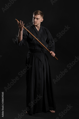 Kendo guru wearing in a traditional japanese kimono is practicing martial art with the shinai bamboo sword against a black studio background.