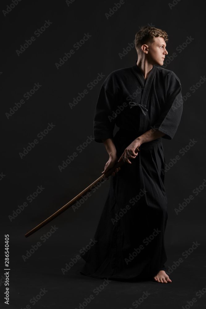 Kendo guru wearing in a traditional japanese kimono is practicing martial art with the shinai bamboo sword against a black studio background. Kendo guru wearing in a traditional japanese kimono is practicing martial art with the shinai bamboo sword against a black studio background.