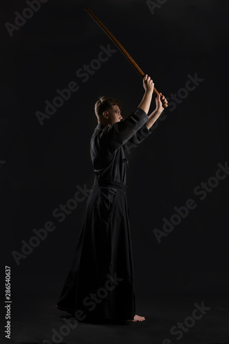 Kendo guru wearing in a traditional japanese kimono is practicing martial art with the shinai bamboo sword against a black studio background. © nazarovsergey
