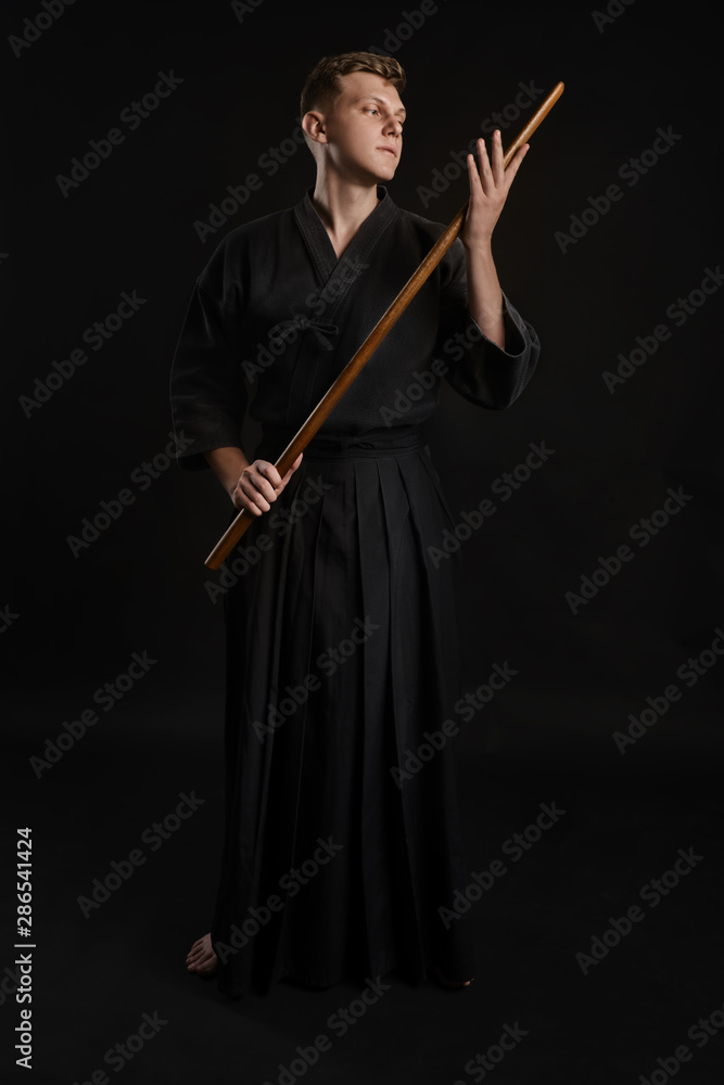 Kendo guru wearing in a traditional japanese kimono is practicing martial art with the shinai bamboo sword against a black studio background. Kendo guru wearing in a traditional japanese kimono is practicing martial art with the shinai bamboo sword against a black studio background.