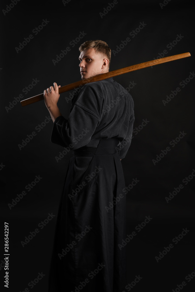 Kendo guru wearing in a traditional japanese kimono is practicing martial art with the shinai bamboo sword against a black studio background. Kendo guru wearing in a traditional japanese kimono is practicing martial art with the shinai bamboo sword against a black studio background.