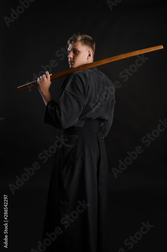 Kendo guru wearing in a traditional japanese kimono is practicing martial art with the shinai bamboo sword against a black studio background.