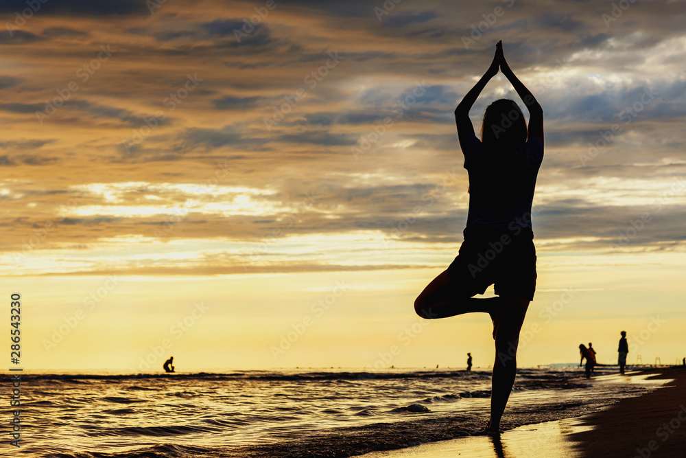 Yogi meditates in a pose of a tree against the background of the sea at beautiful sunset time
