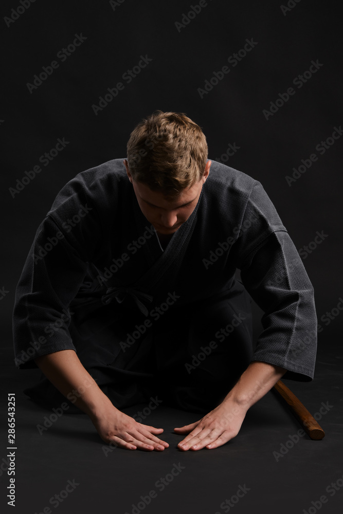 Kendo guru wearing in a traditional japanese kimono is practicing martial art with the shinai bamboo sword against a black studio background. Kendo guru wearing in a traditional japanese kimono is practicing martial art with the shinai bamboo sword against a black studio background.