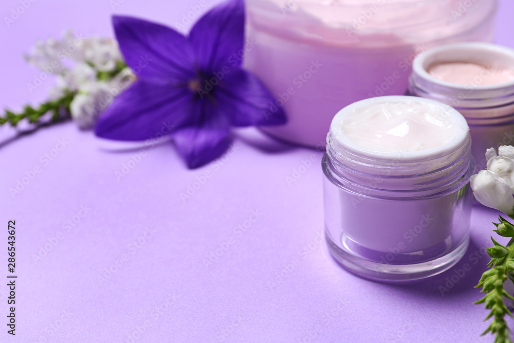 Jars of body cream and flowers on lilac background. Space for text Jars of body cream and flowers on lilac background. Space for text