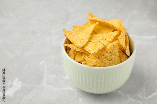 Bowl with tasty Mexican nachos chips on grey table, space for text