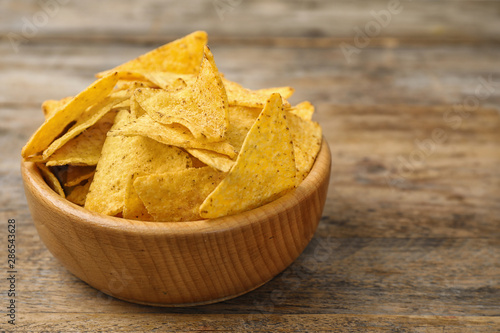 Bowl with tasty Mexican nachos chips on wooden table, space for text