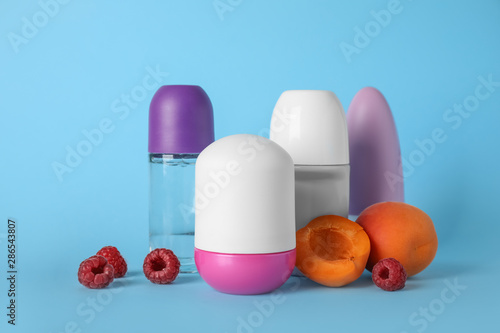 Different female roll-on deodorants, apricots and raspberries on light blue background